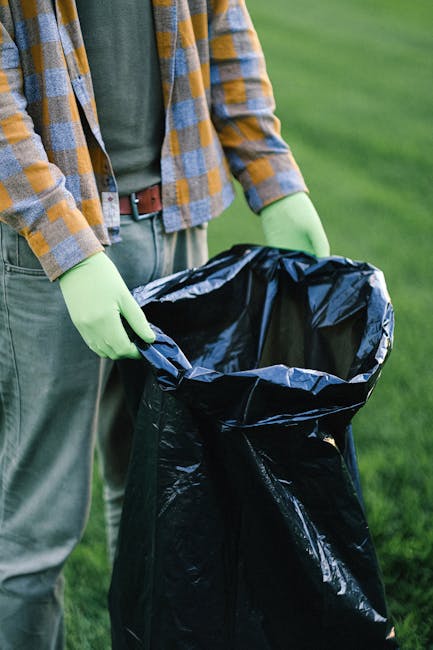 A photograph of a variety of discarded waste materials arranged outdoors on a paved surface. The collection includes a large, black plastic rubbish bag filled with unknown contents, situated towards t